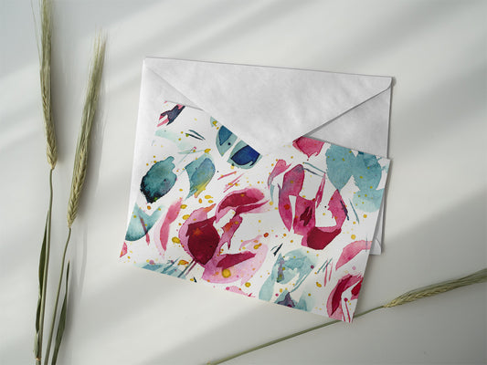 Product photo of abstract watercolor greeting card titled "Joy and Sorrow" with various blue, green, and red hues on a clean, white card. The card is laying on top of an envelope on a white background next to greenery.