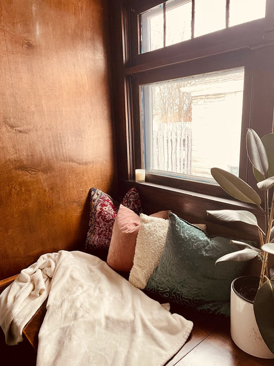 a cozy window nook with colorful cushions and a potted plant