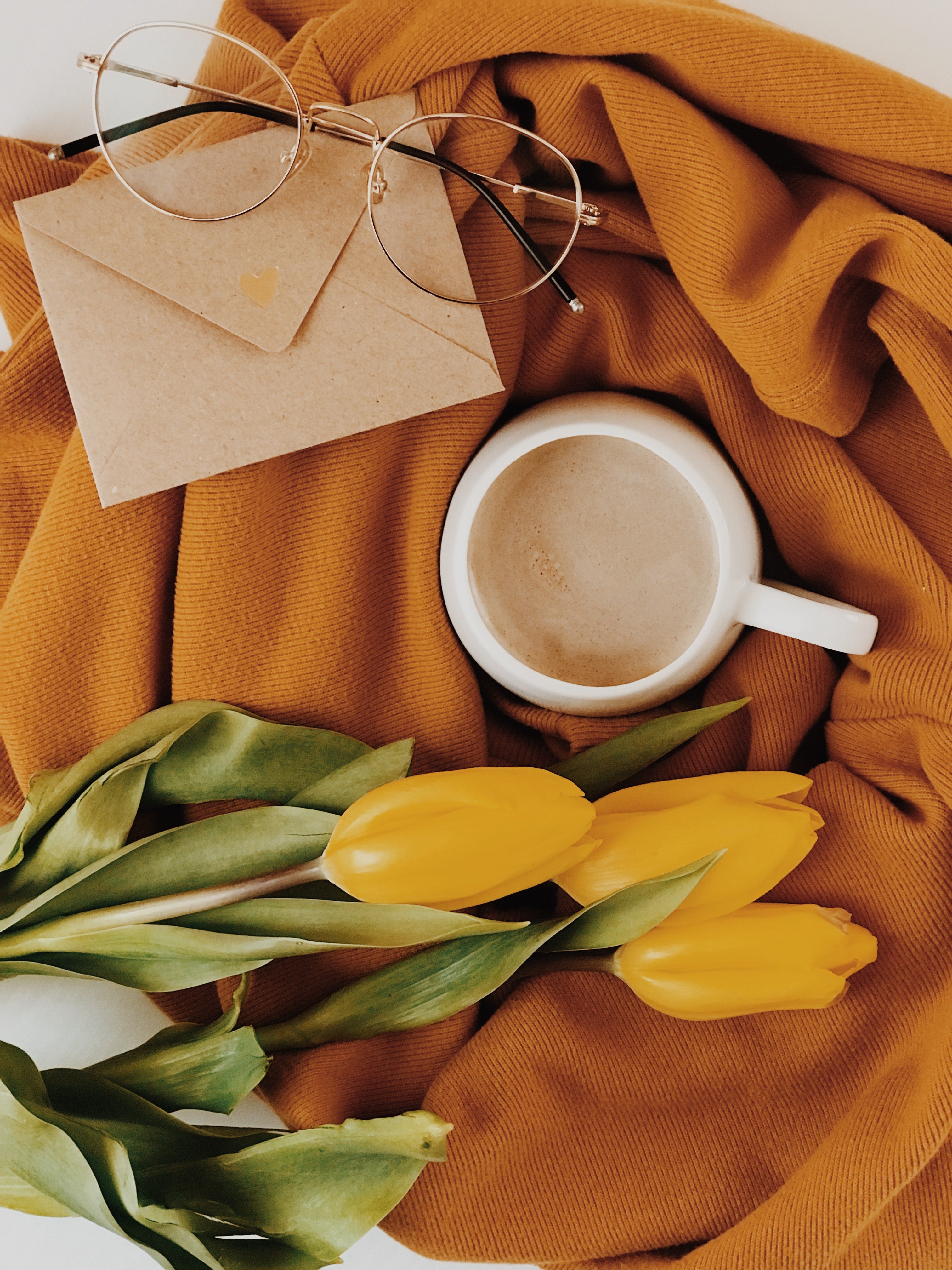 Yellow Tulips, coffee, a tan envelope, and glasses sitting on an orange blanket